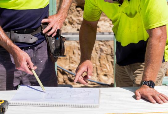 Two workers in high visibility shirts looking at housing plans