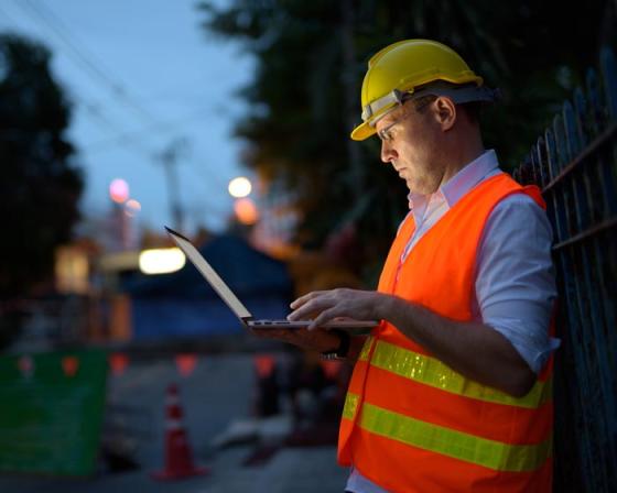 Certifier looking at plans on laptop at building site in the evening.